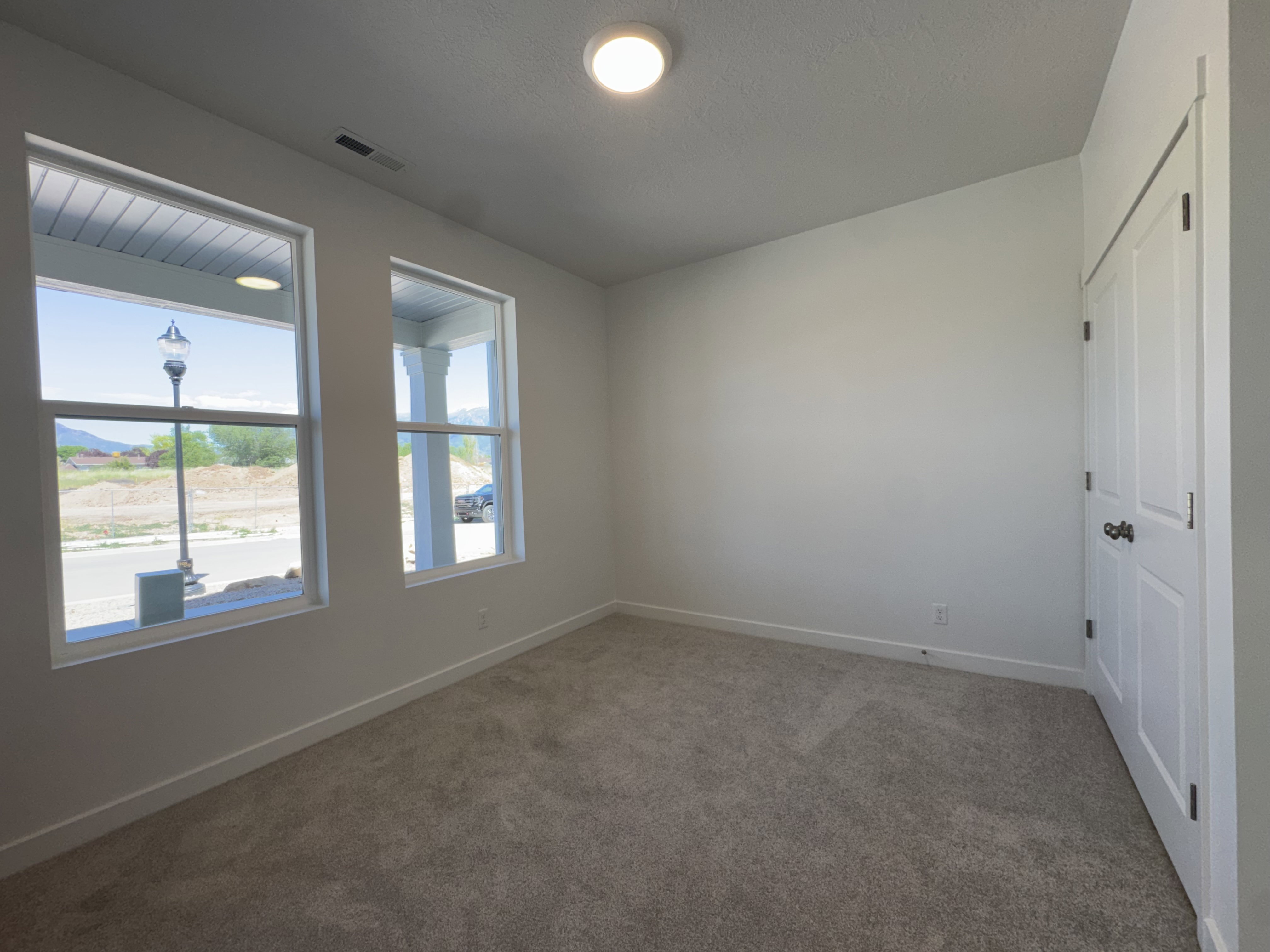 Carpeted room with two large windows, a flush-mount ceiling light, and a two-panel door with black hardware