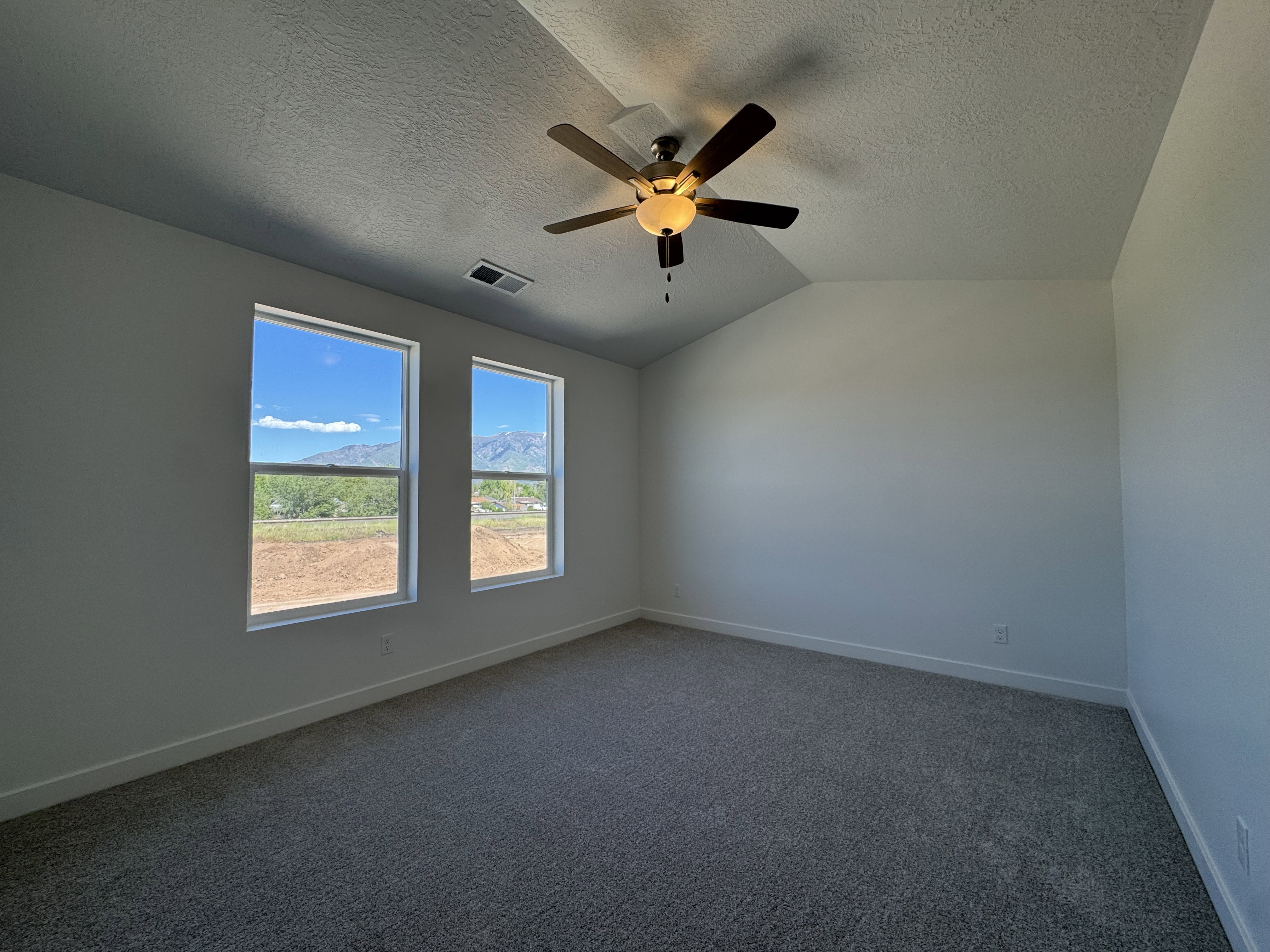 Bright interior space featuring two large windows, a ceiling fan with integrated lighting, and vaulted ceilings