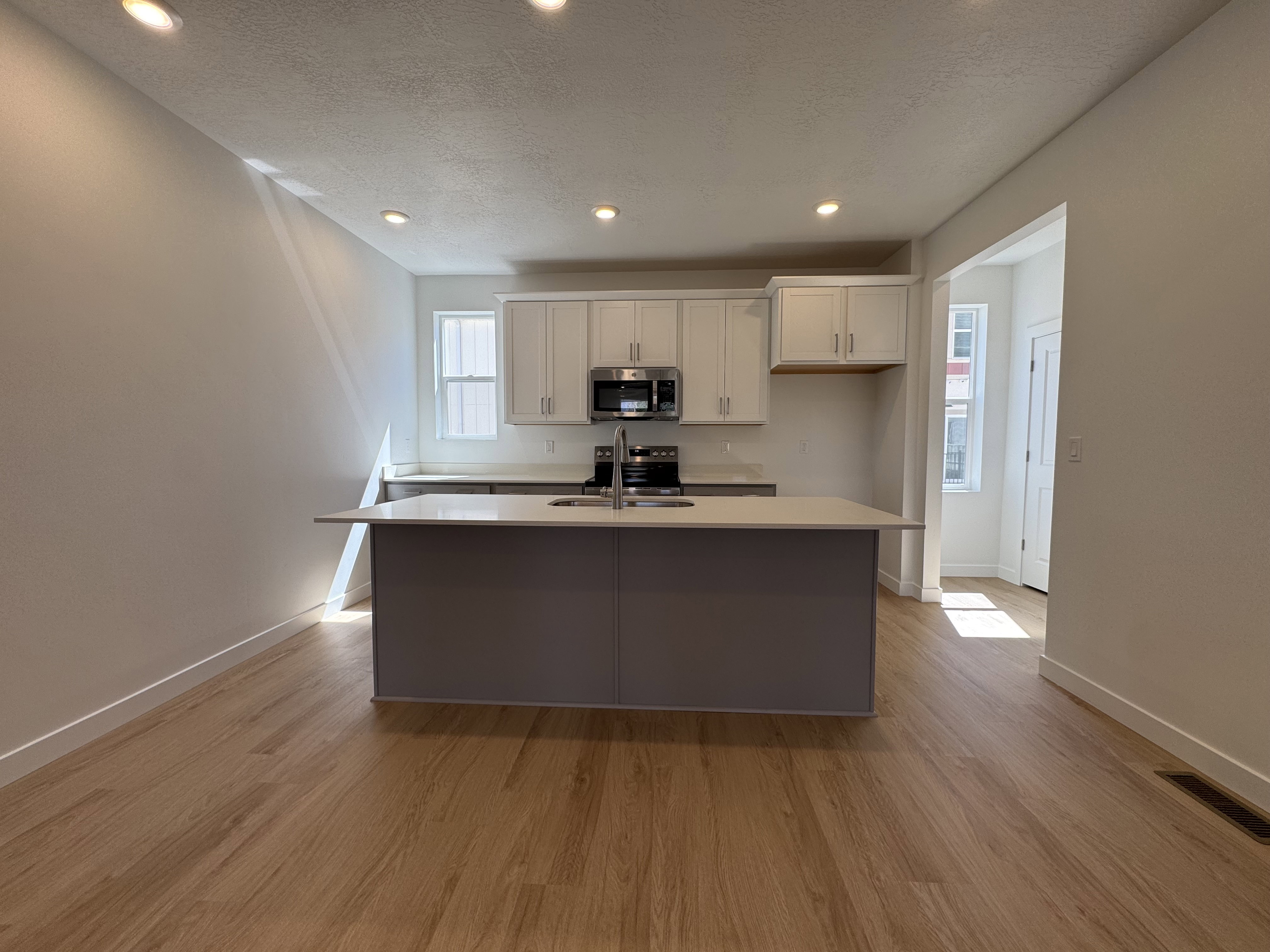 Kitchen featuring a central island with an integrated sink, stainless steel appliances, upper cabinetry, recessed lighting, and wood-finish flooring