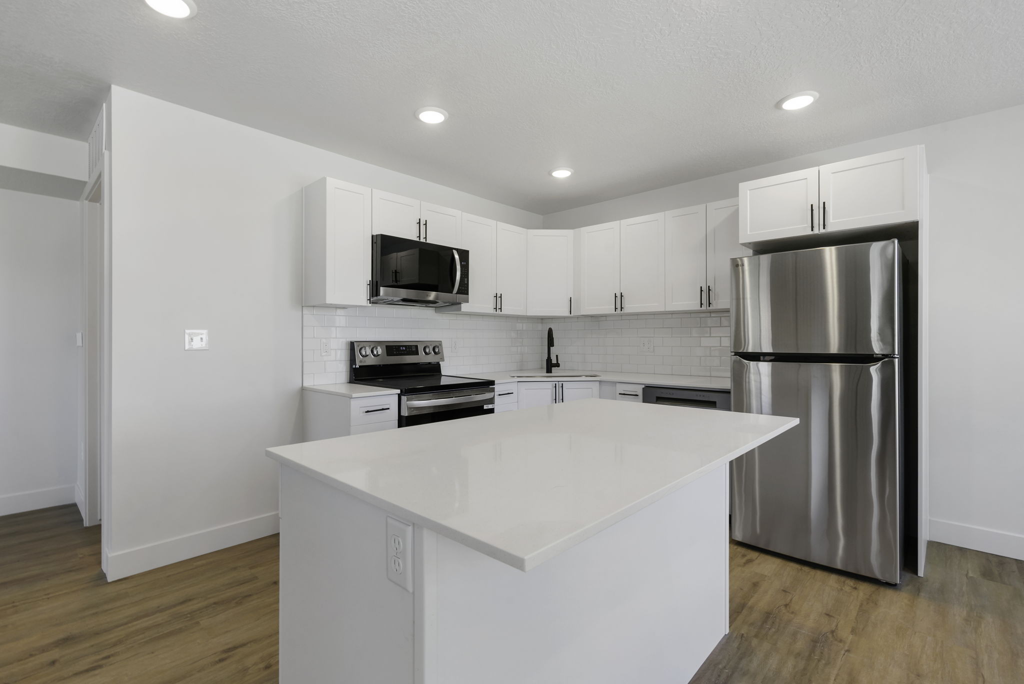 Kitchen featuring a white quartz-top island, white cabinetry, stainless steel appliances, a white subway tile backsplash, and wood-finish flooring