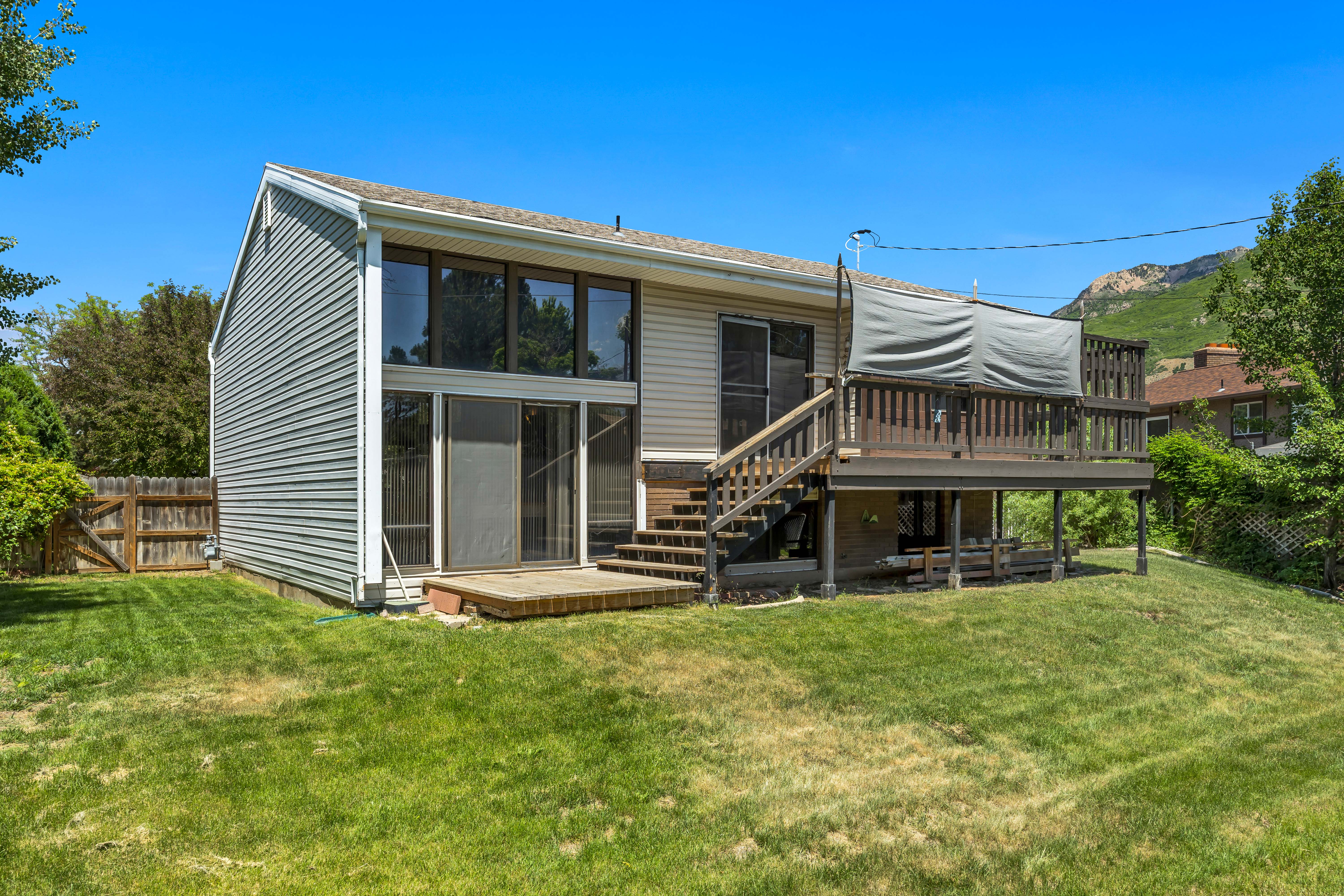 Rear exterior featuring a spacious elevated deck with wooden railings, a ground-level patio, and a wall of windows
