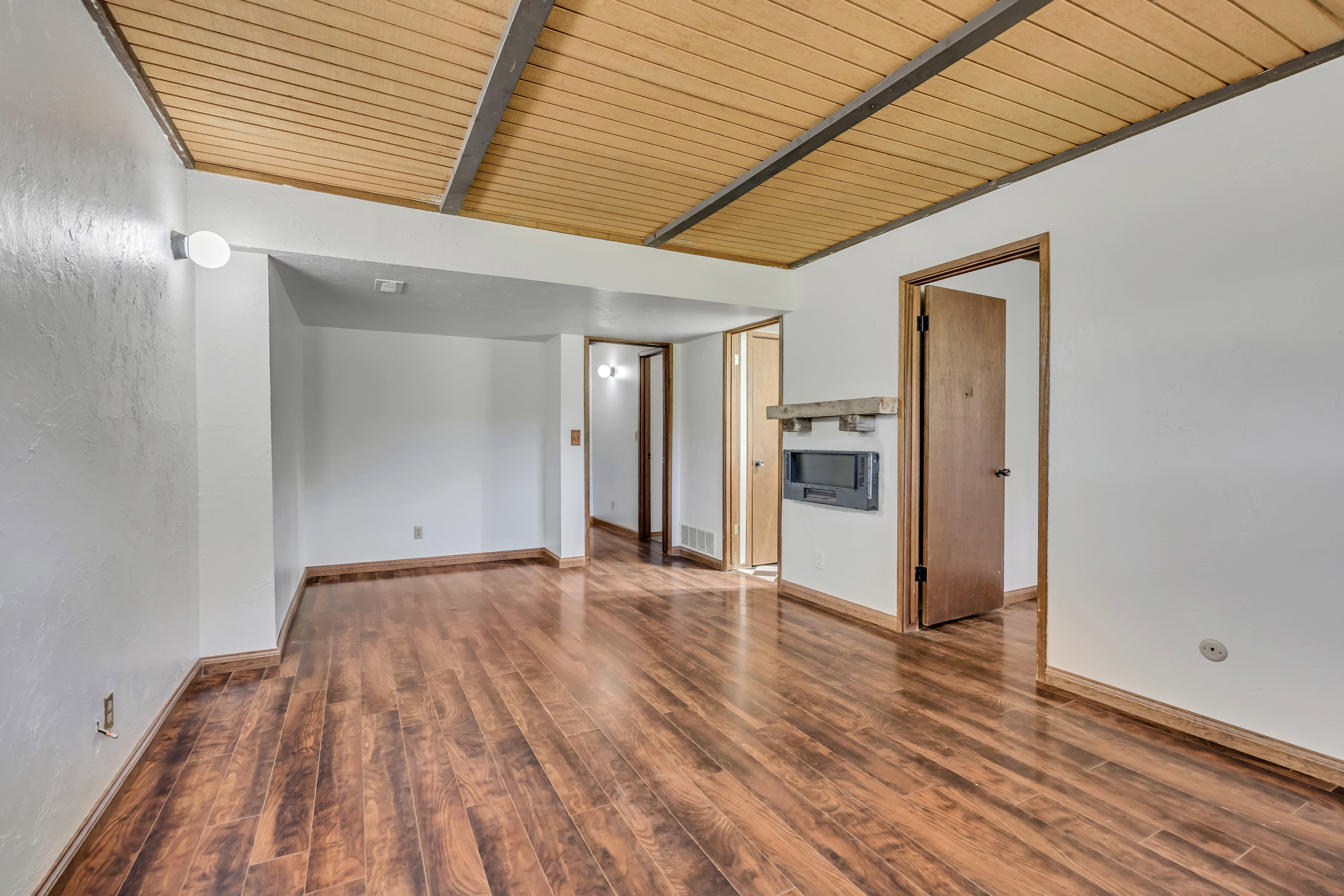 Spacious room featuring wood-finish flooring, a wood-paneled ceiling with exposed beams, and a built-in fireplace