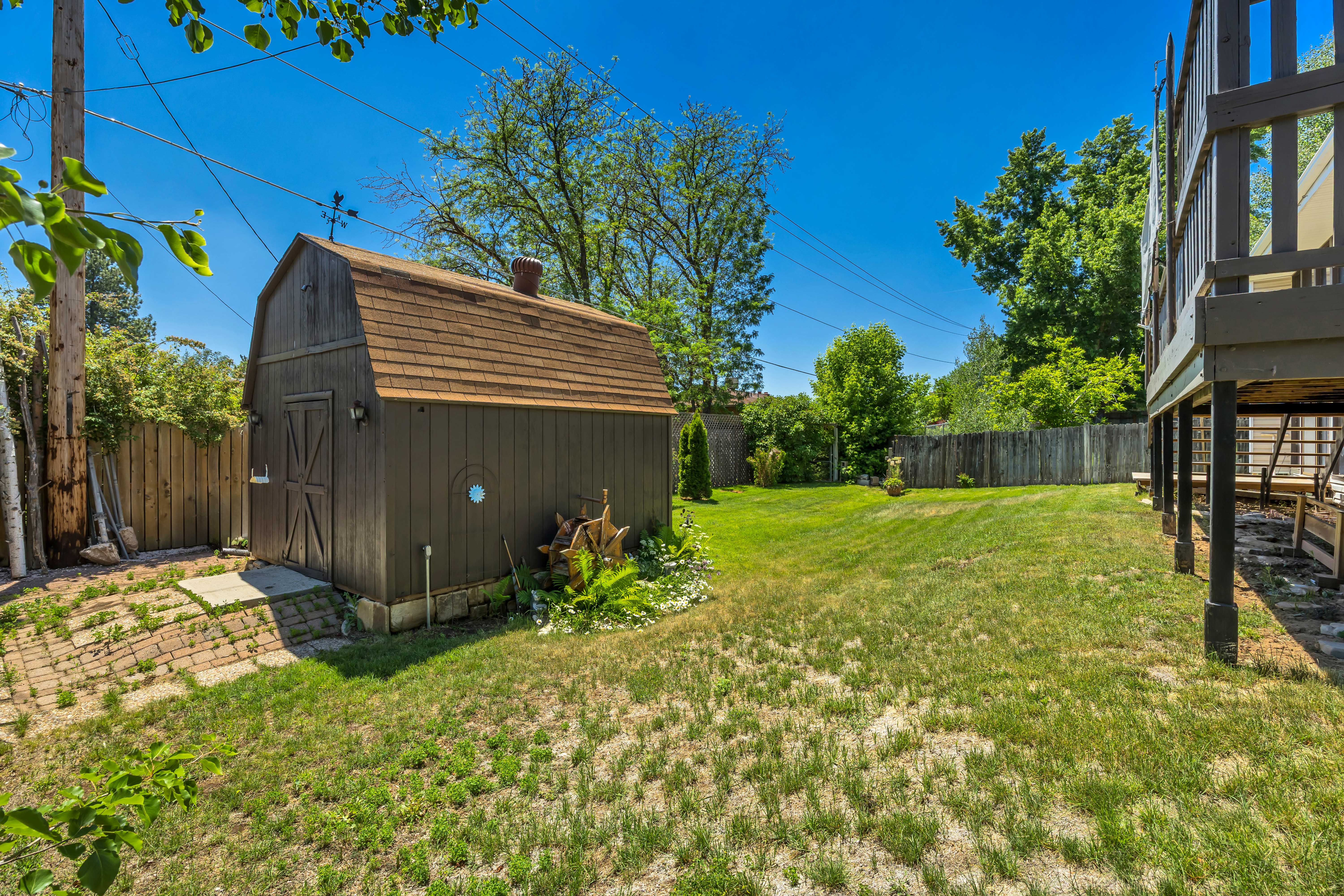 Generous backyard featuring a large barn-style shed with shingle roofing and exterior lighting, a wooden privacy fence, and a spacious lawn area