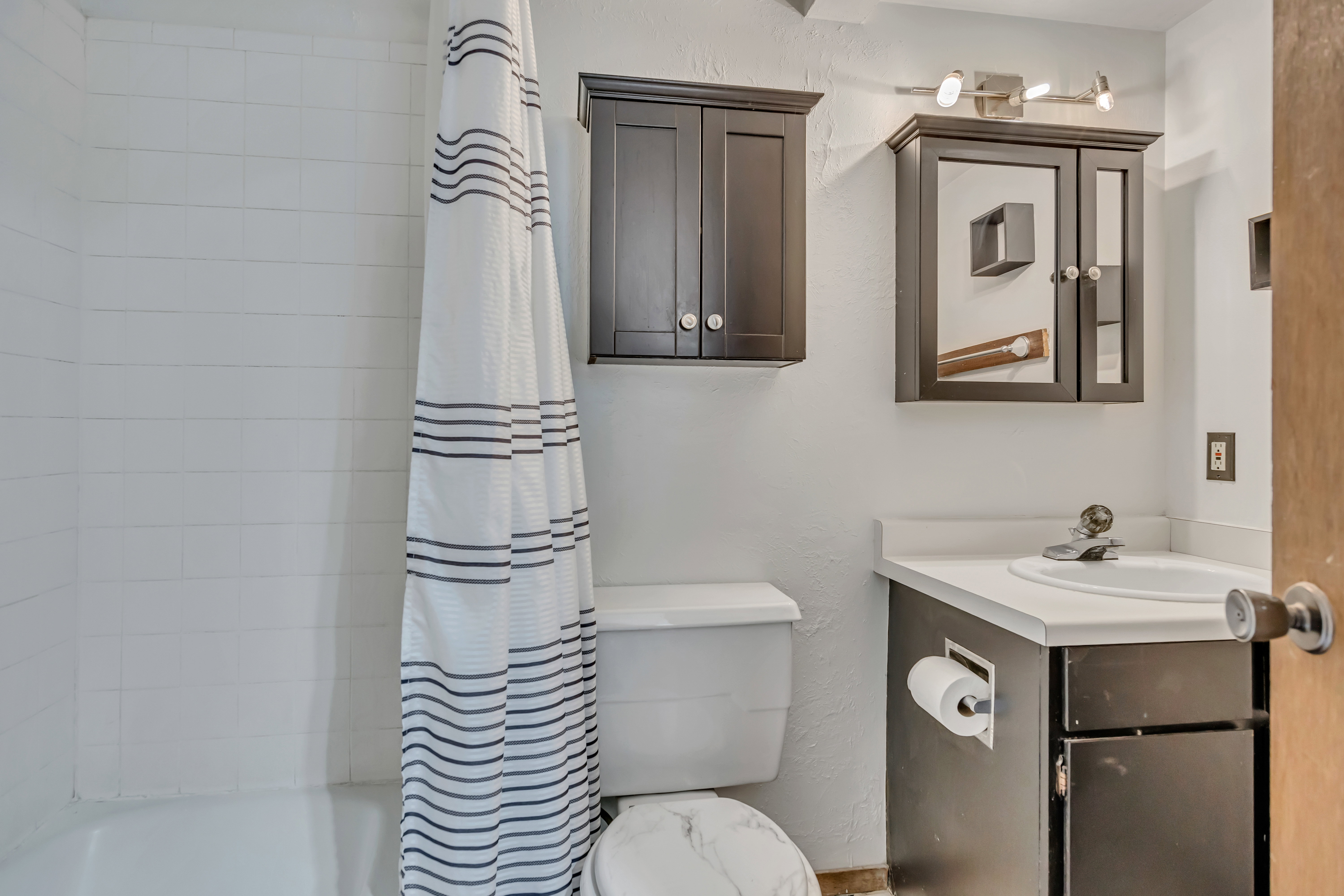 Bathroom featuring a white subway tile shower surround, dark wood-finish vanity with an integrated sink, white countertop, dark wood-finish medicine cabinet, and coordinating wall-mounted storage cabinet