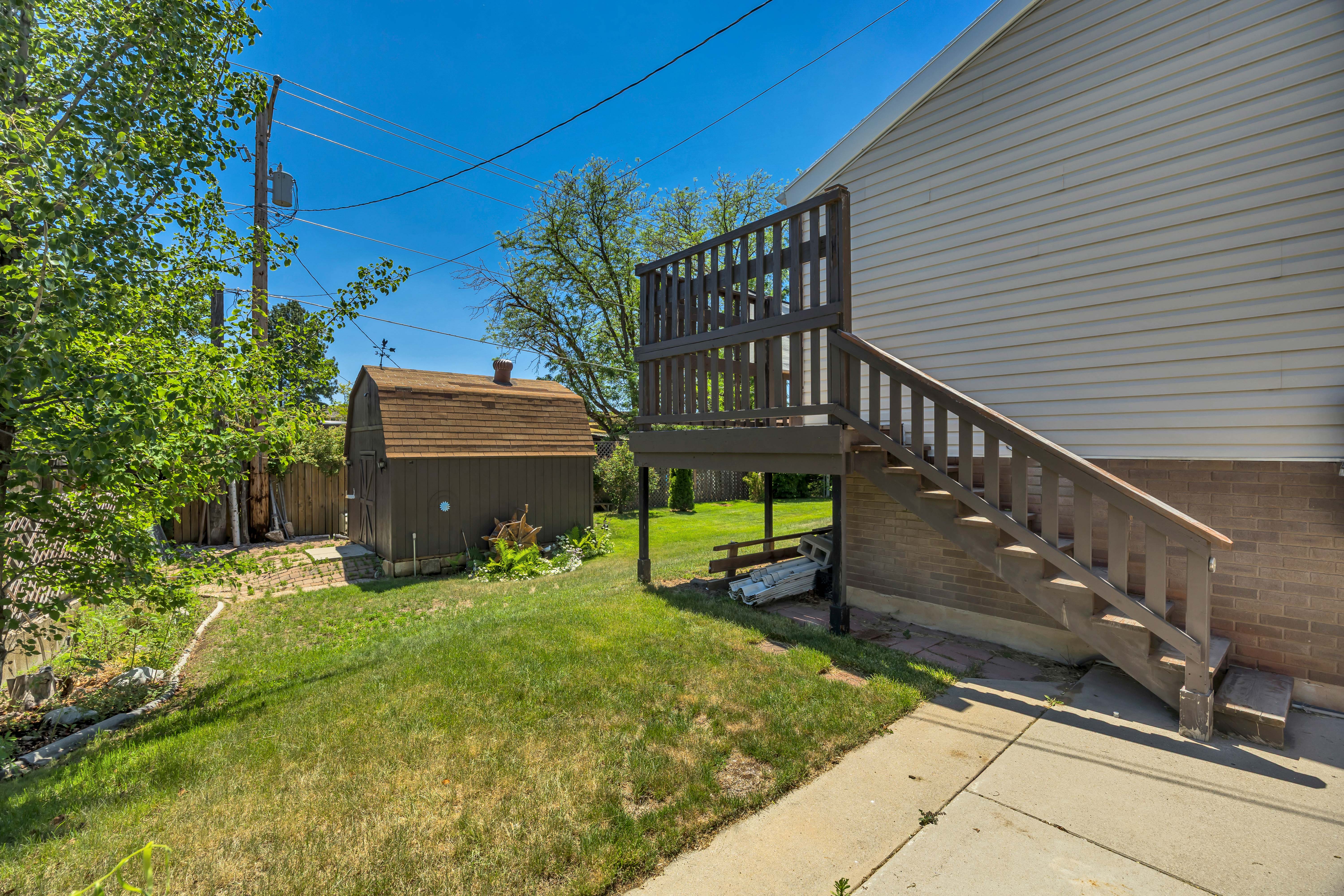Exterior siding featuring a wooden deck with railing and stairs, a grass lawn, and a barn-style shed