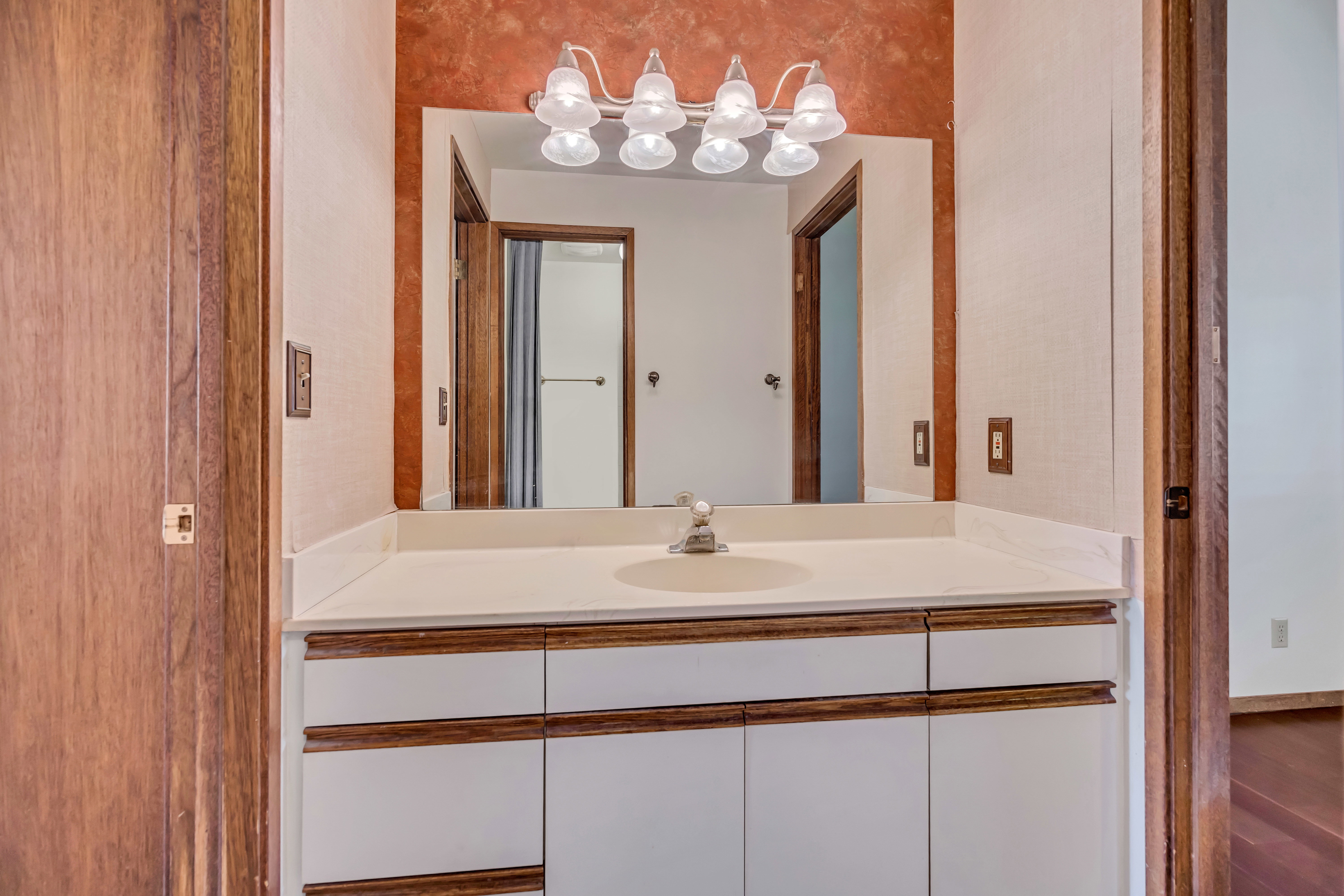 Vanity with an integrated sink, white countertop, and white cabinetry featuring wood-finish accents
