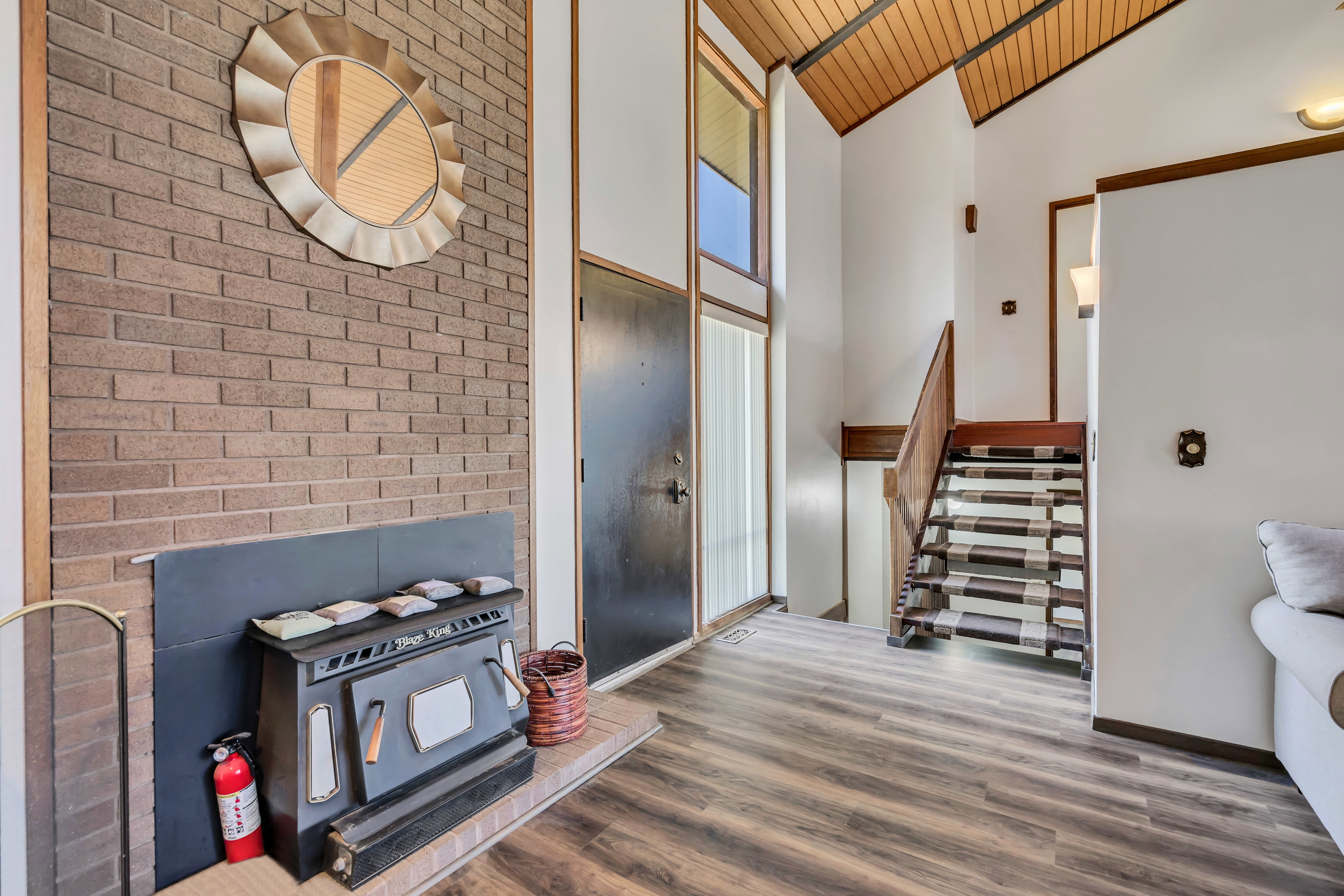 Vaulted ceiling with wood-finish paneling, brick fireplace with hearth, and wood-finish flooring