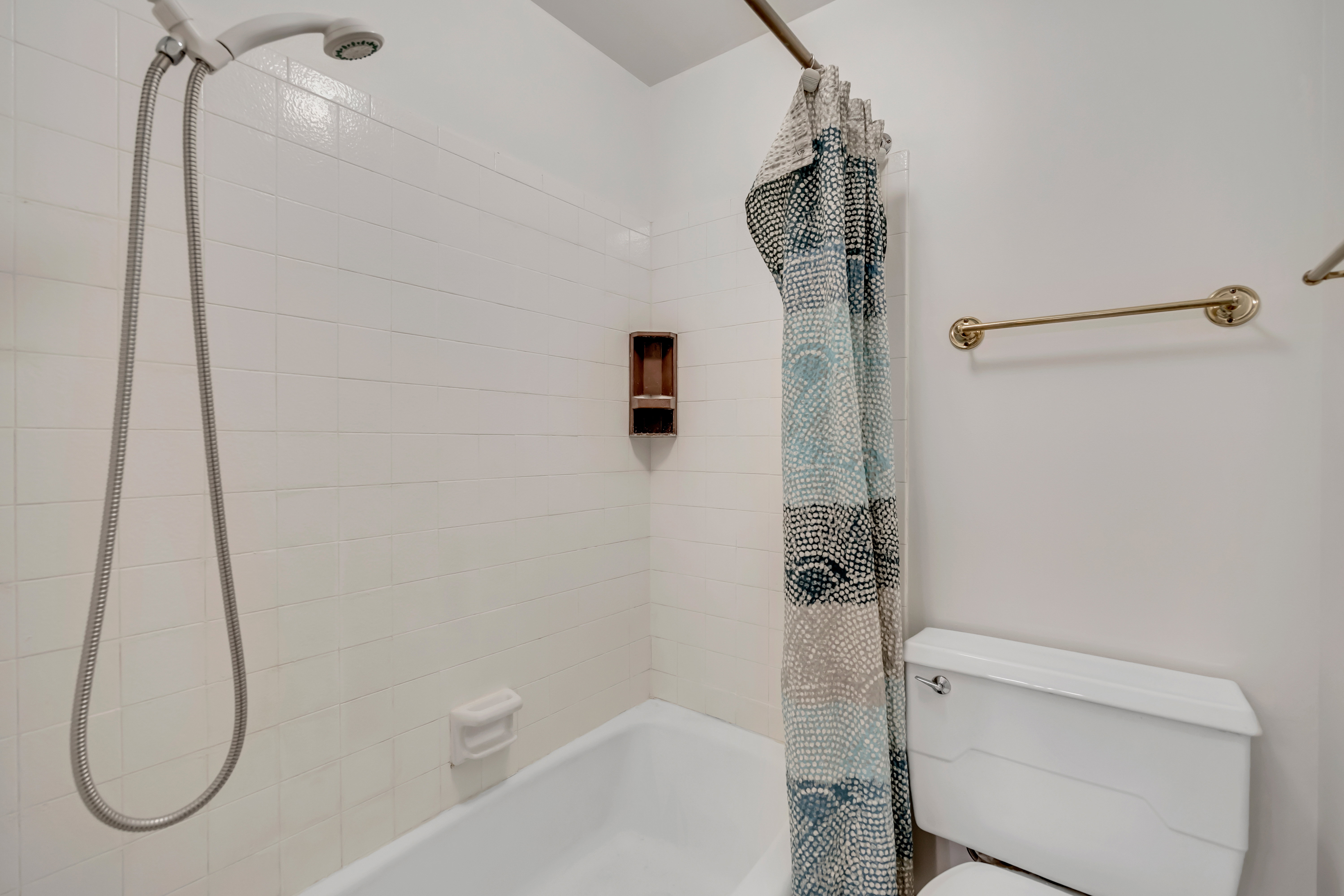 Bathtub and shower combination featuring white subway tile surround, recessed wall niche, and handheld shower fixture