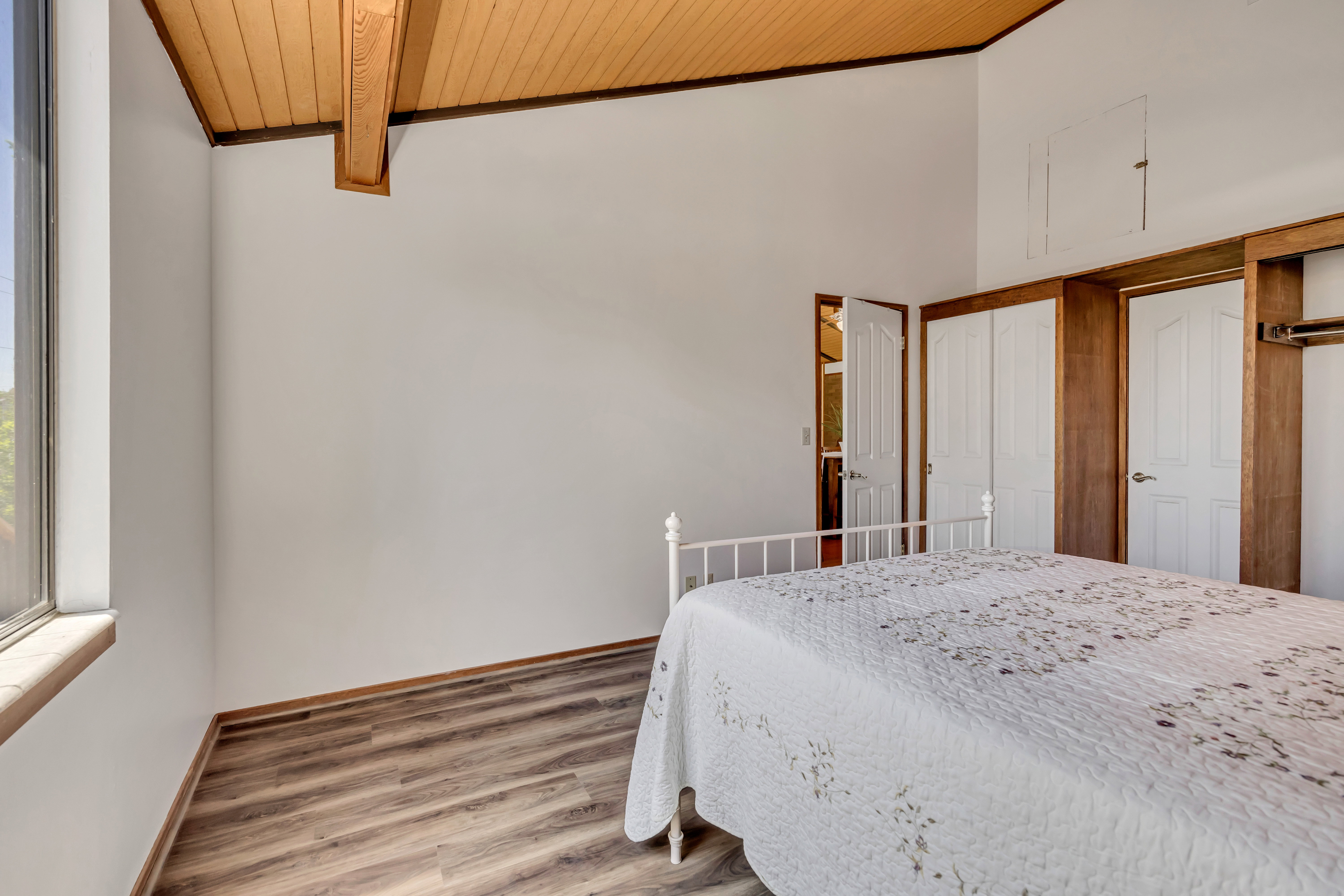 Vaulted wood-paneled ceiling with exposed beam, wood-finish flooring, full-lite window, built-in wooden shelving, and white paneled doors