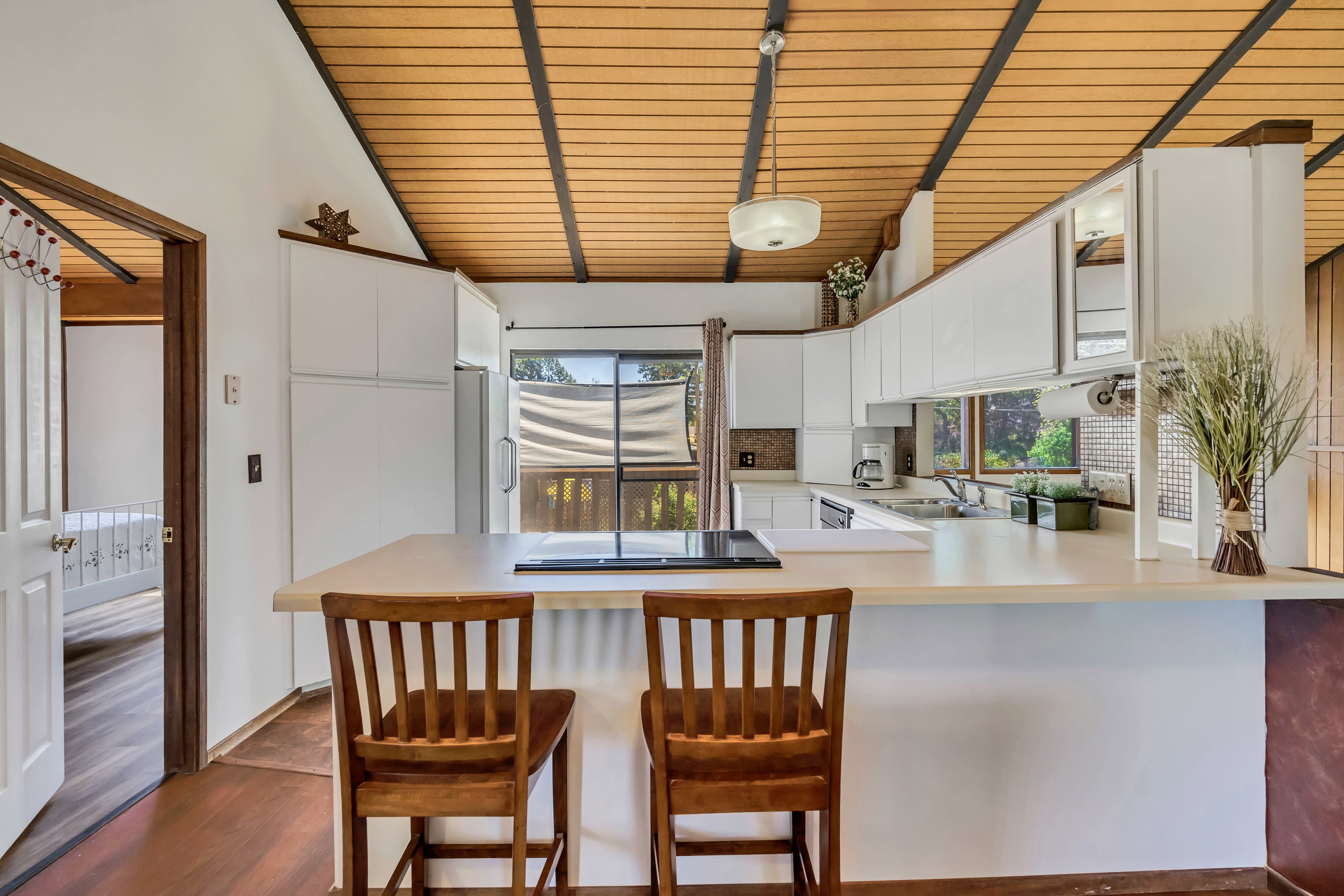 Kitchen featuring a wood-panel vaulted ceiling with exposed beams, white upper and lower cabinetry, and a peninsula countertop with integrated cooktop