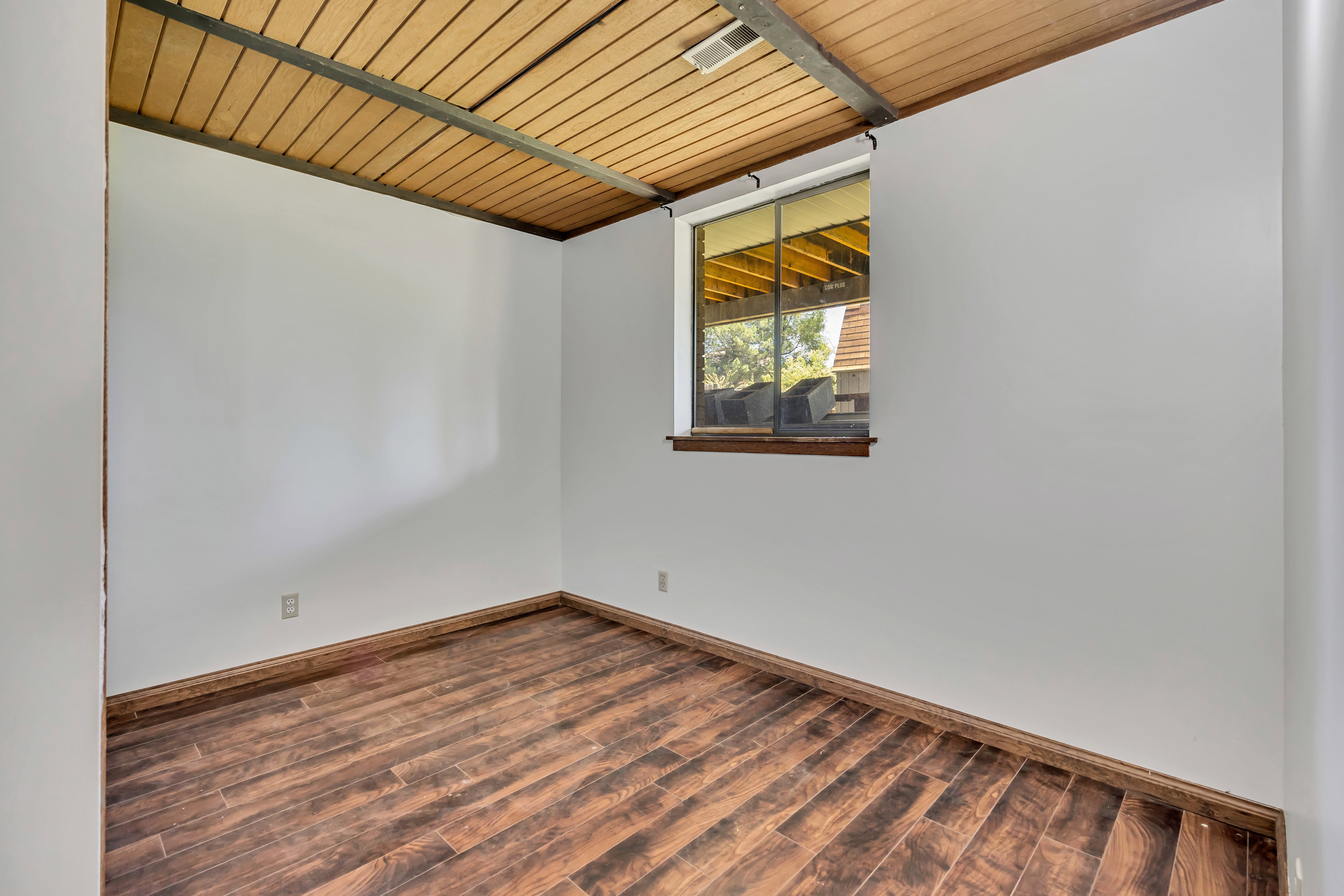 Room featuring wood-finish flooring, white walls, and a wood-paneled ceiling with exposed beams