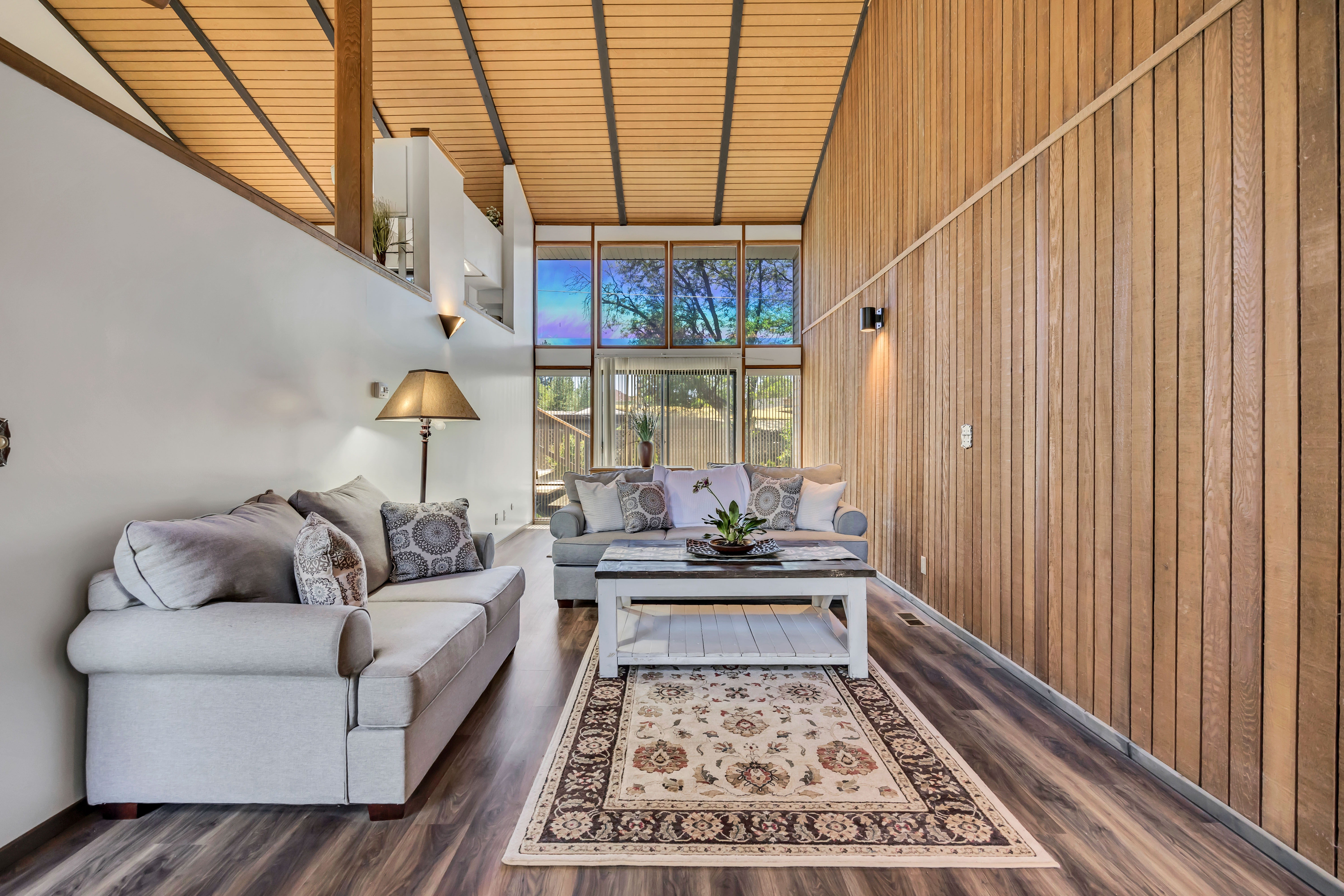 Living area featuring high ceilings with exposed beams, wood-finish flooring, and a vertical wood-paneled accent wall