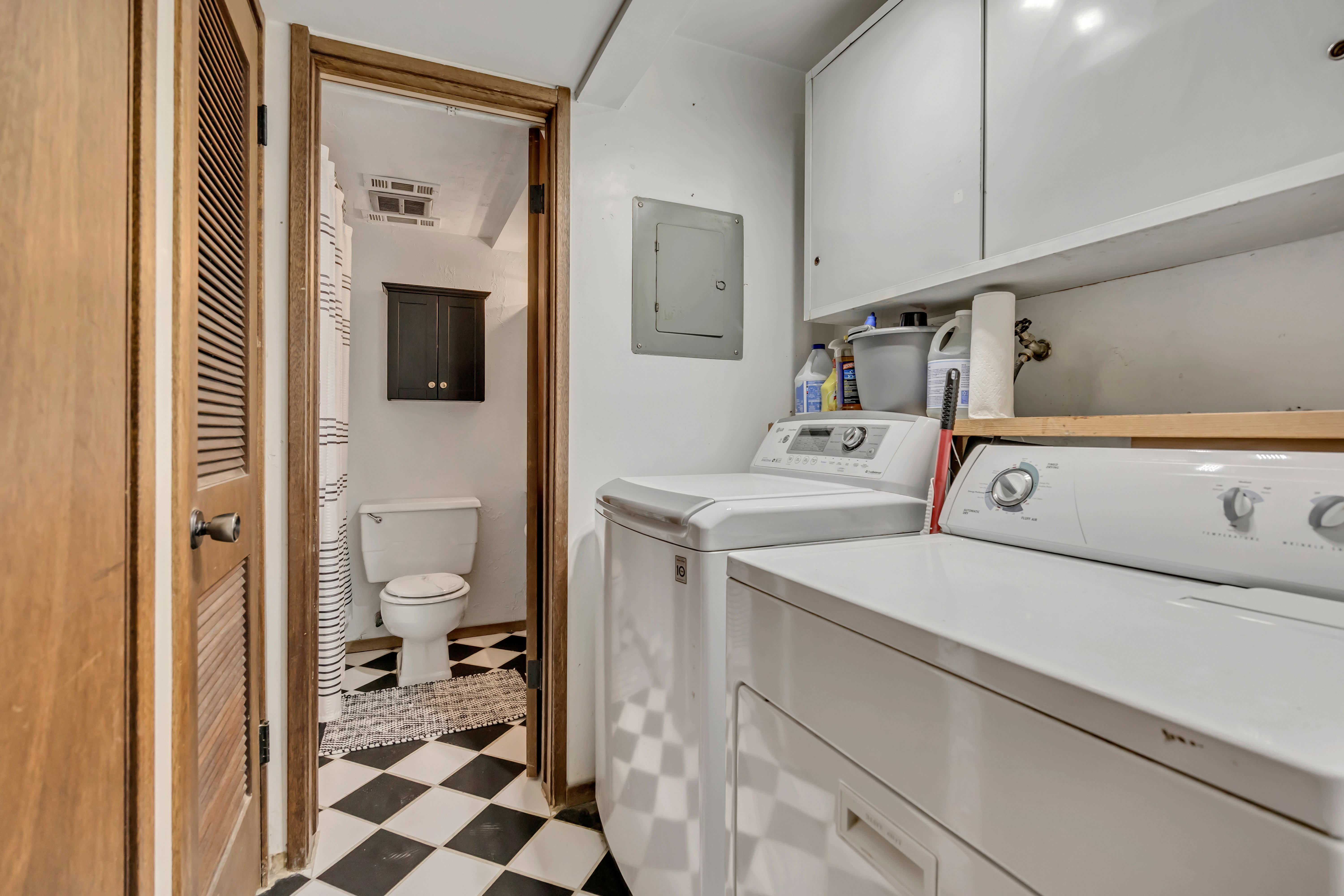 Utility area featuring built-in white cabinetry, an exposed electrical panel, and a wooden shelf