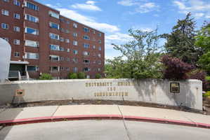 Multi-story brick condominium building featuring numerous window units and a concrete entrance wall with gold lettering