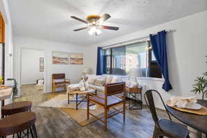 Living area with wood-finish flooring, a large window, and a ceiling fan