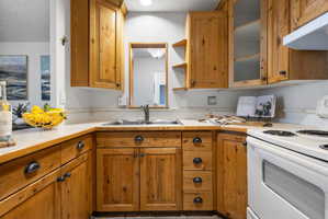 U-shaped kitchen featuring wood-finish cabinetry, a stainless steel sink with a chrome faucet, light-toned countertops, and a white electric range