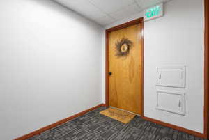 Entryway featuring a wood-panel door with dark trim, contrasting white walls, and geometric pattern carpeting