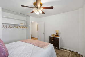 Bedroom featuring a ceiling fan with light fixture, built-in open closet shelving and hanging rod, and light wood-finish flooring