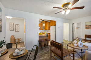 Living area featuring wood-finish flooring, a ceiling fan with integrated lighting, and an open pass-through to the kitchen