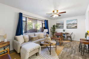 Open concept living area featuring wood-finish flooring, a large picture window, and a ceiling fan