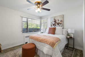 Bedroom featuring wood-finish flooring, a ceiling fan with integrated lighting, and multiple windows with horizontal blinds