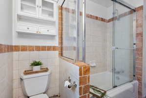 Bathroom featuring a white bathtub, glass shower doors, and a tiled surround