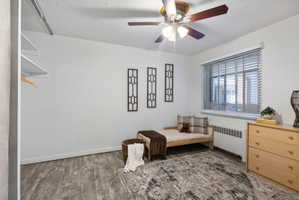 Bright room featuring wood-finish flooring, a ceiling fan with integrated lighting, window with horizontal blinds, and baseboard heating unit