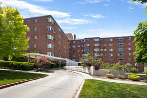 Multi-story brick facade building featuring a covered drive-through entrance, mature landscaping, and a paved circular driveway