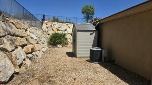 Rear yard featuring a rock retaining wall, gravel ground cover, and a storage shed