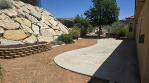 Exterior patio area featuring a curved concrete walkway, a stone retaining wall, and natural rock landscaping
