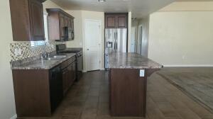 Kitchen featuring a central island with a granite-style countertop, dark wood-finish cabinetry, tile backsplash, and stainless steel appliances