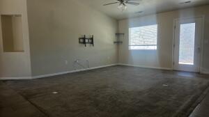 Spacious room featuring vaulted ceilings, a ceiling fan with integrated lighting, dark carpeting, and a glass-paneled exterior door