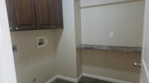 Laundry area featuring upper cabinetry with dark wood-finish doors, a built-in shelf with a stone-look surface, neutral wall paint, and tiled flooring