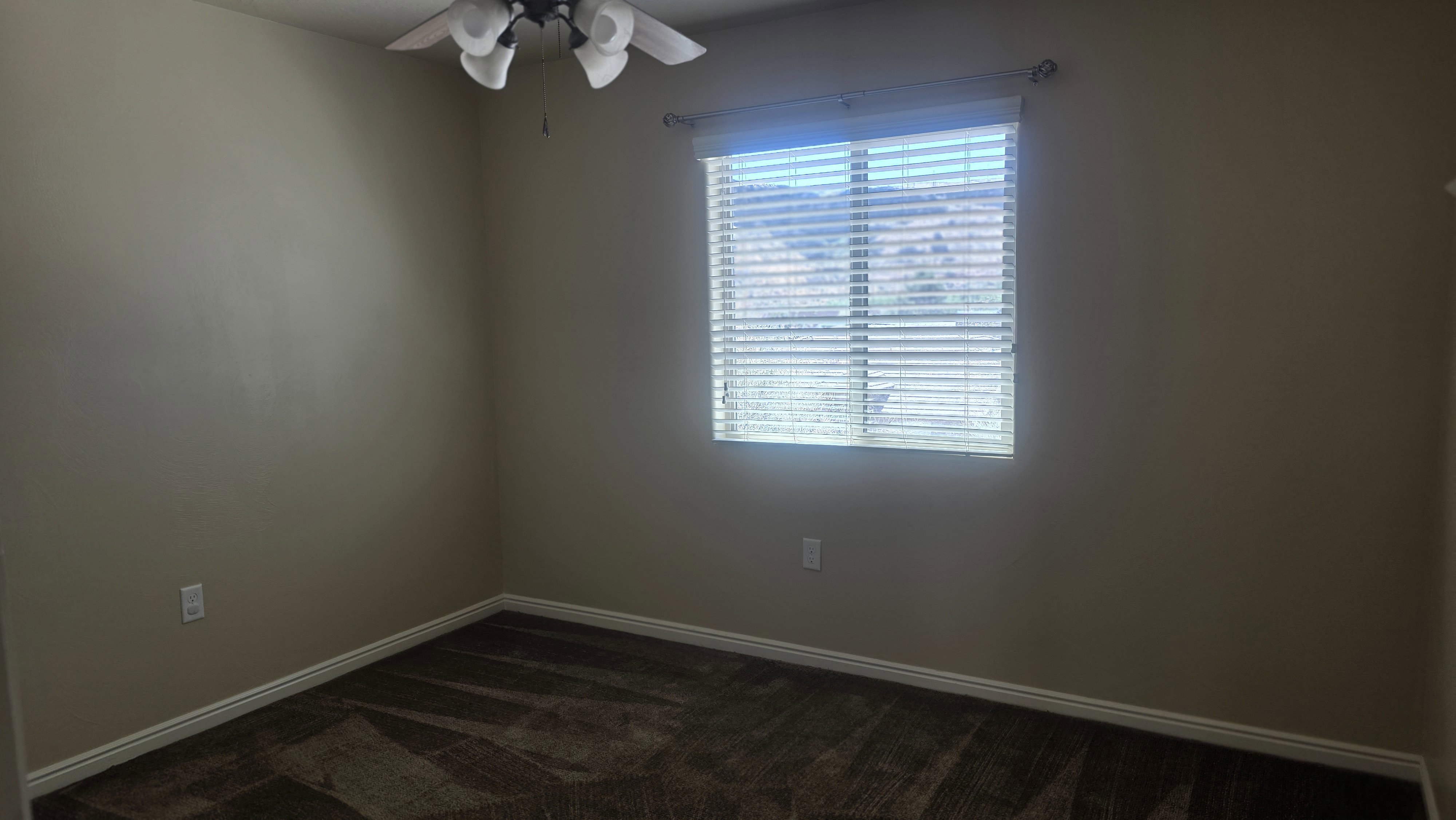 Room with neutral-toned walls, patterned carpet flooring, a window with horizontal blinds, a ceiling fan, and white baseboards