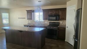 Kitchen featuring a central island with a light-toned countertop, wood-finish cabinetry, a patterned backsplash, and stainless steel appliances including a range and microwave