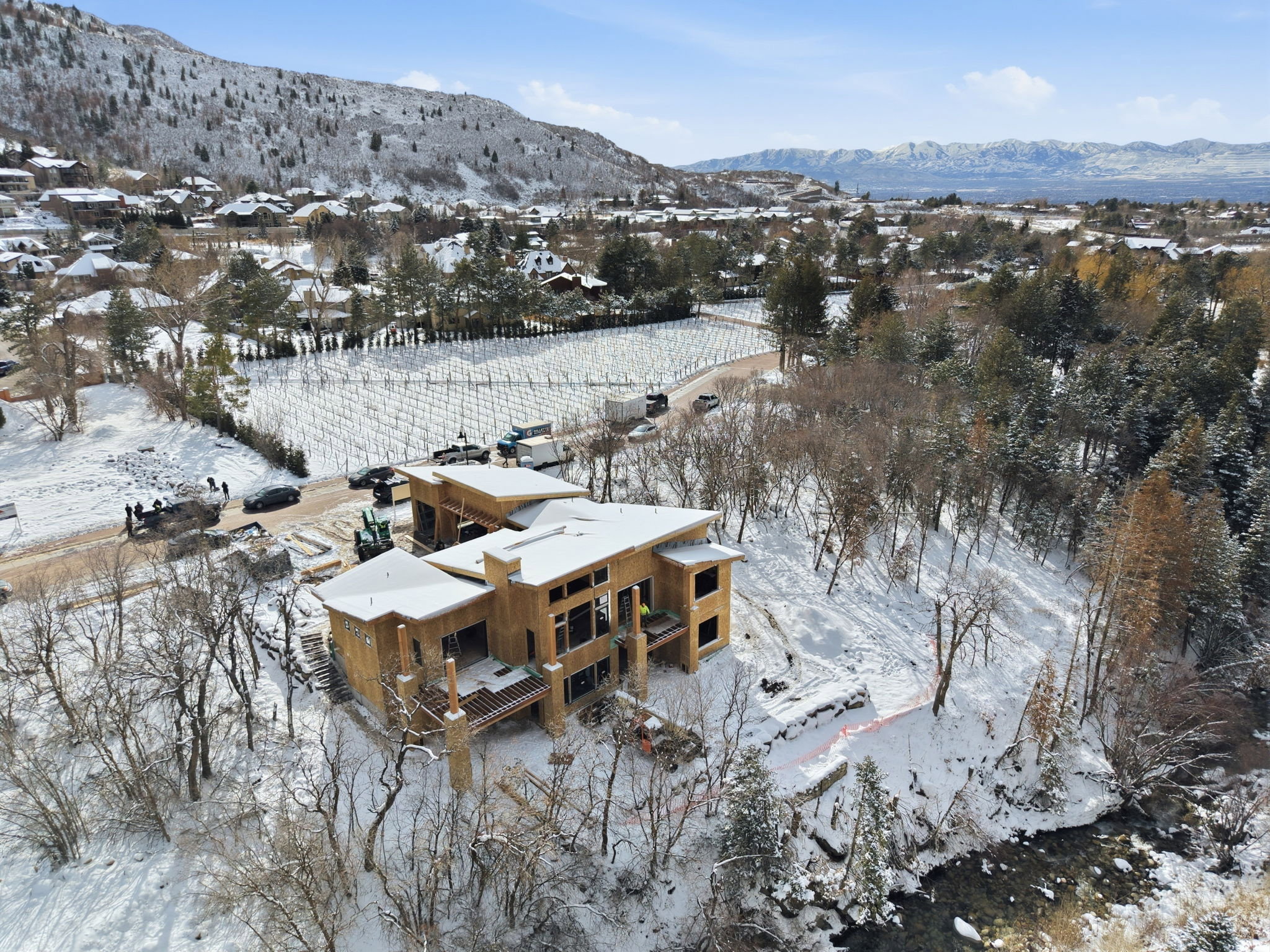 Expansive wood-framed structure with multiple levels and large window openings, complemented by a nearby natural water feature