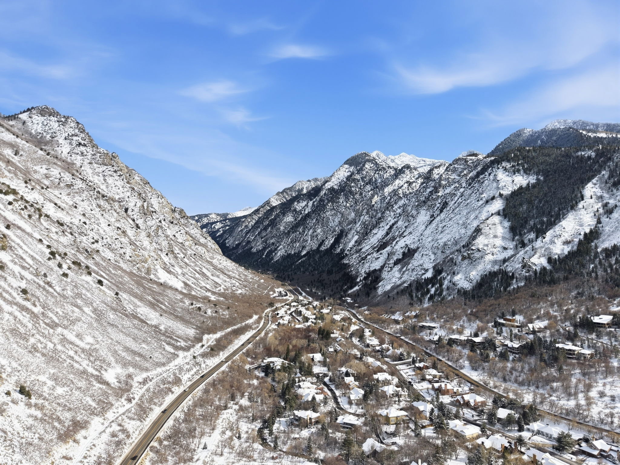 Mountain landscape featuring snow-dusted peaks, a winding roadway, and a community of residential structures