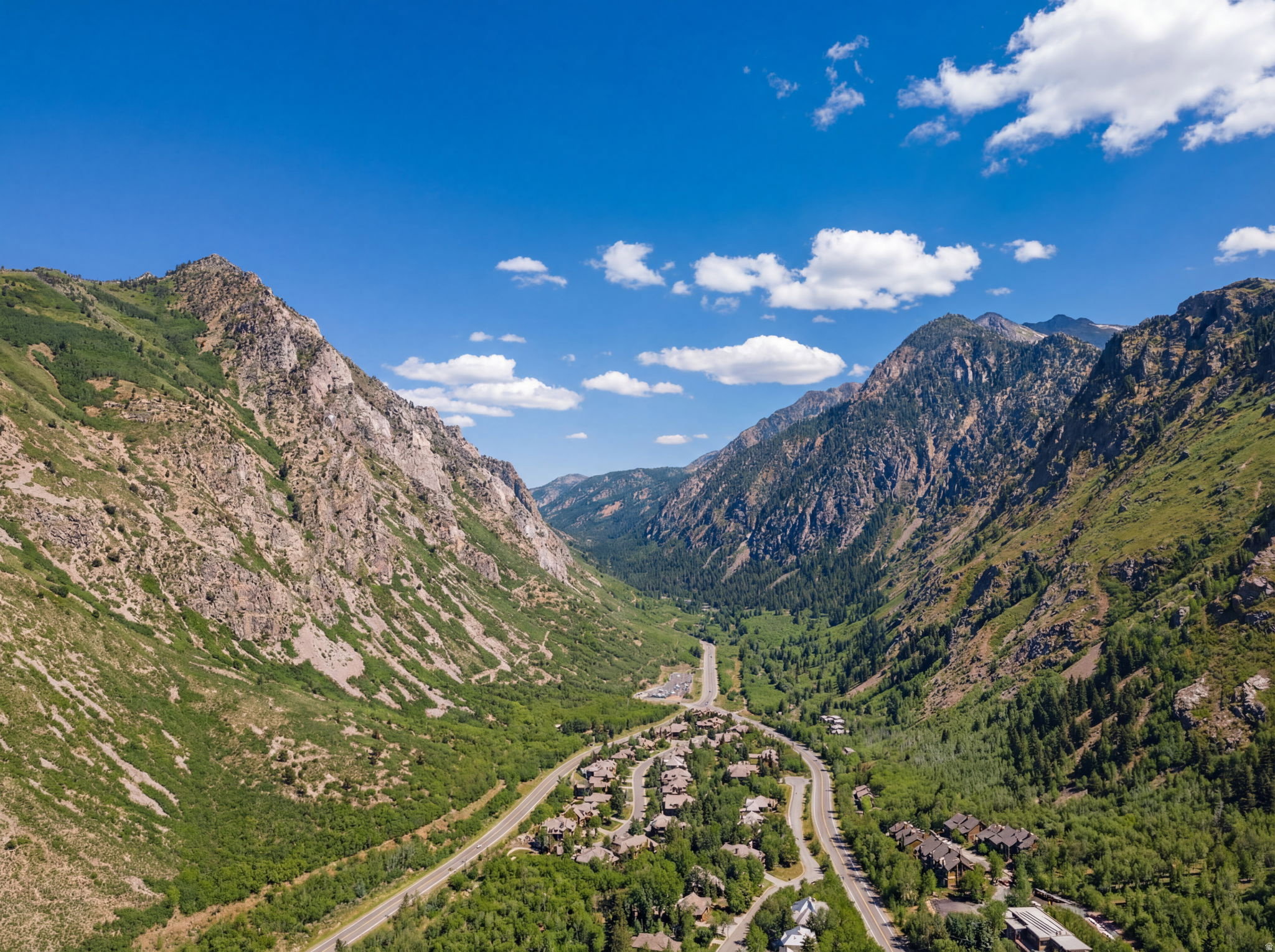 Mountain valley setting featuring a winding road, extensive tree coverage, and a collection of residential structures