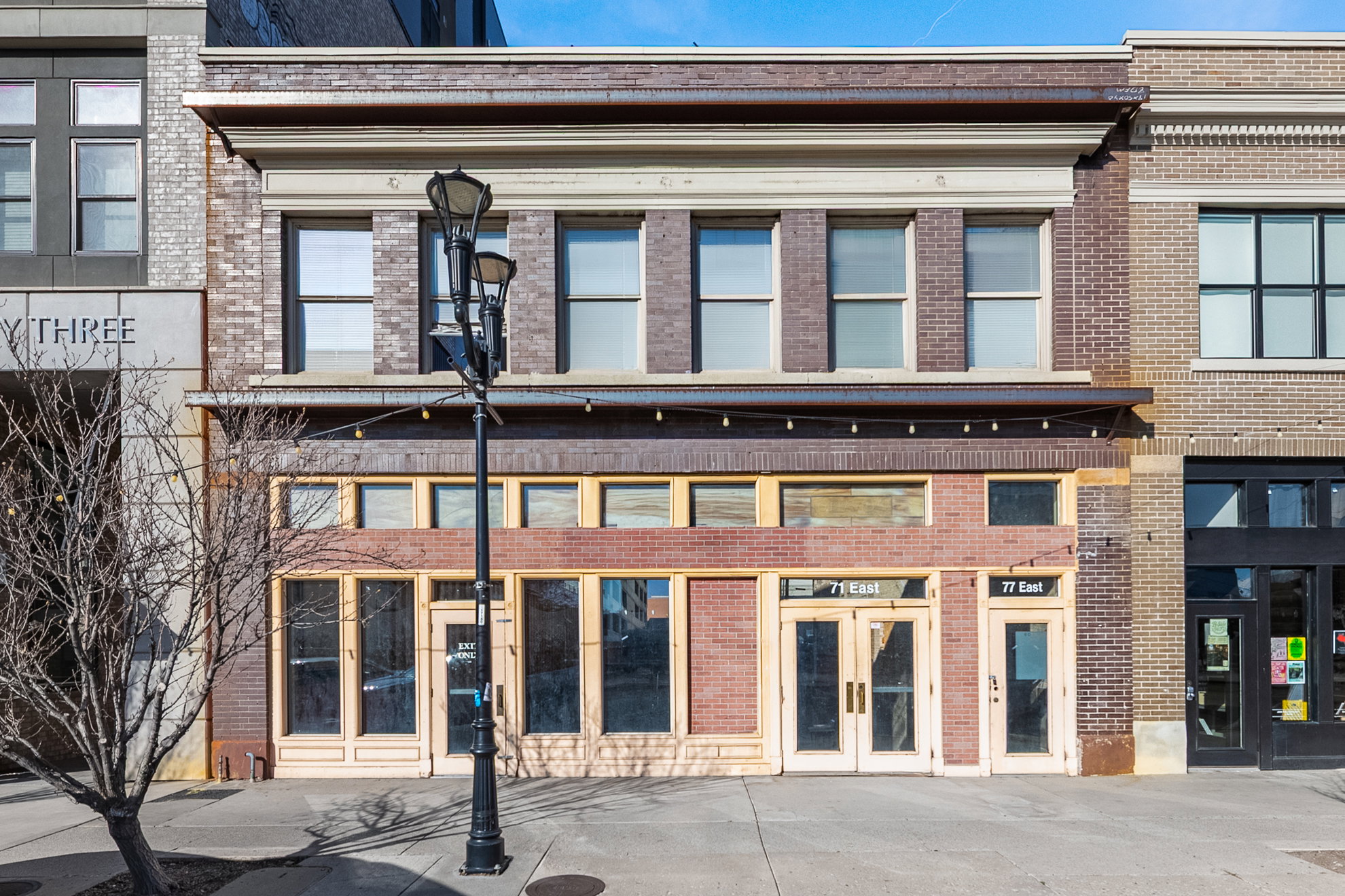 Brick facade building featuring a prominent storefront with multiple large windows, recessed entryways, and upper-level windows