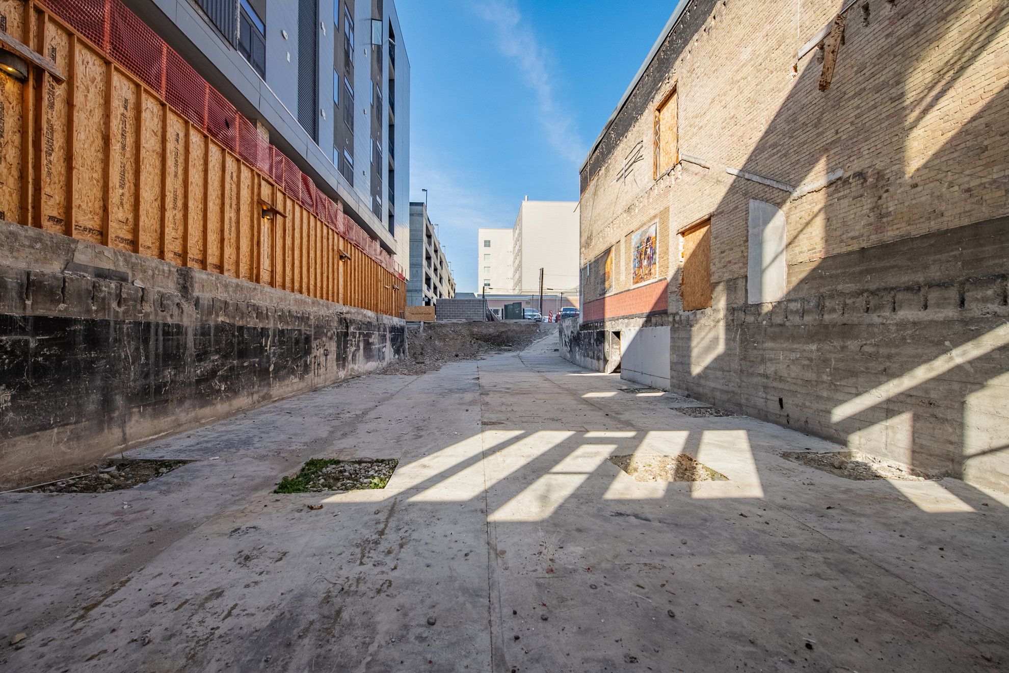 Concrete access path bordered by a multi-story structure with modern facade elements and a traditional brick building