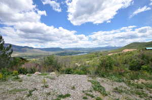 Expansive mountain landscape featuring broad valleys, a distant body of water, and evergreen trees