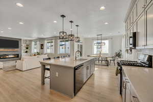 Spacious open-concept kitchen featuring a large island with sink, stainless steel appliances, light cabinetry, and light wood-finish flooring