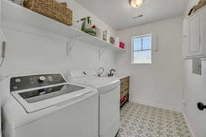 Laundry room featuring patterned tile flooring, a window with decorative security bars, and open shelving