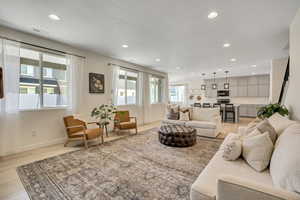 Open-concept living area featuring light wood-finish flooring, recessed lighting, multiple windows, and a staircase with a dark handrail