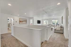 Open loft area featuring neutral-toned carpet flooring, recessed lighting, and white painted walls
