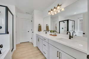 Dual vanity with undermount sinks and dark bronze fixtures, light-toned wood-finish flooring, white paneled doors with dark hardware, and a large mirror with a multi-bulb light fixture