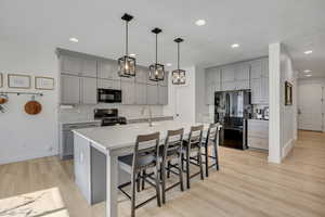 Kitchen featuring light gray cabinetry, a white countertop island with seating for four, stainless steel appliances, and wood-finish flooring