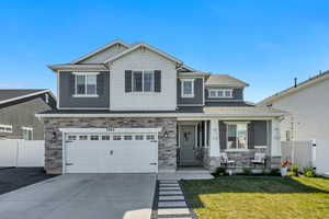 Two-story residence featuring a stone and siding facade, covered front porch, an attached two-car garage, concrete driveway, and a front lawn with a decorative stone pathway
