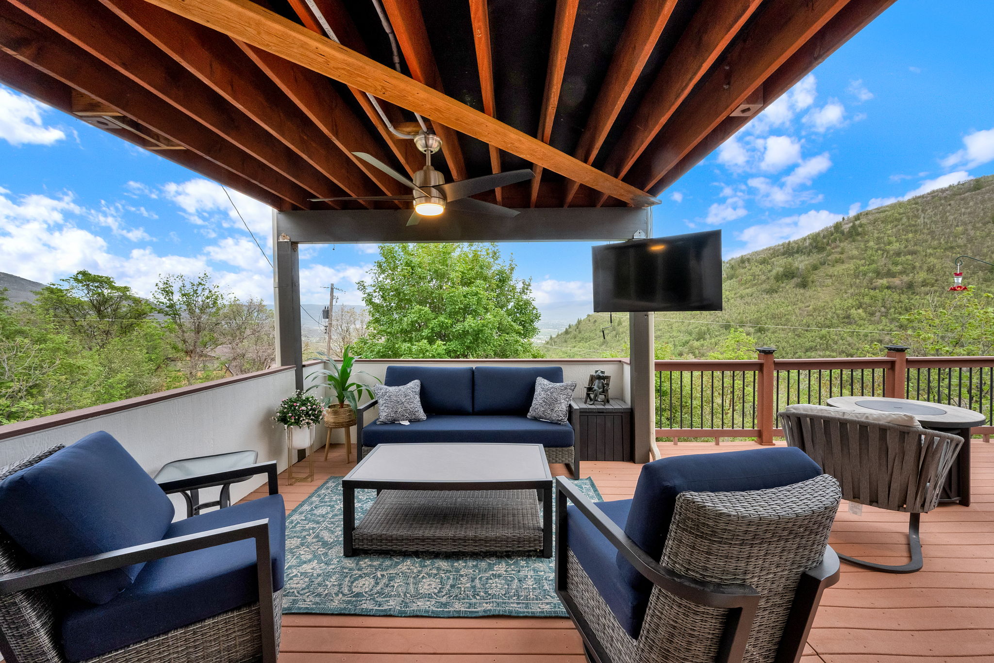 Spacious outdoor patio featuring a wood-finish ceiling, mounted television, ceiling fan, and composite decking