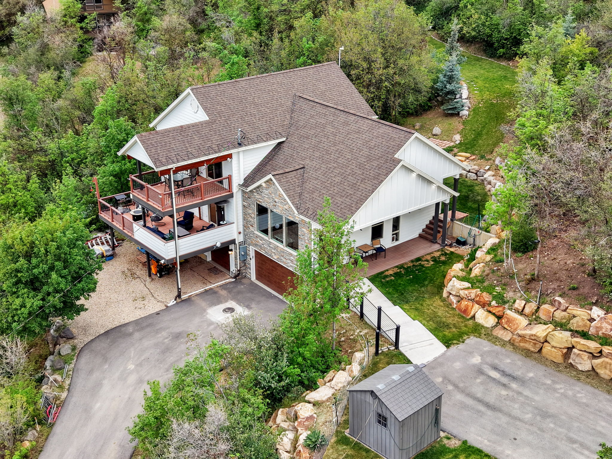 Multi-level residence featuring a stacked deck, stone and horizontal siding exterior, and a two-car garage with a wood-finish door
